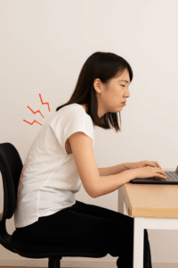 デスクワーク中に背中を丸めて座る日本人女性、猫背姿勢による腰への負担を示すイメージ写真